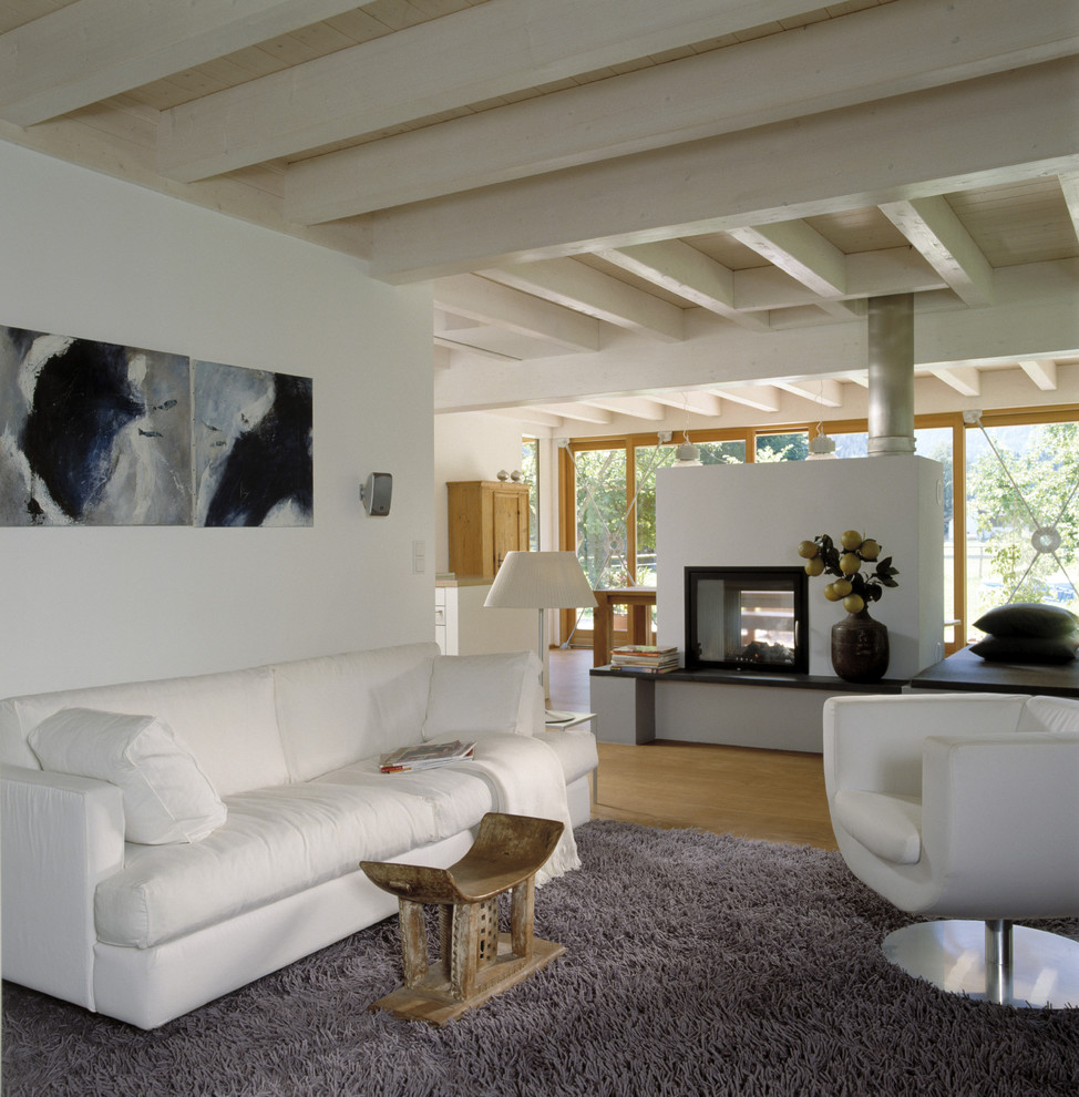 Mittelgroßes, Offenes Modernes Wohnzimmer mit weißer Wandfarbe, hellem Holzboden, Tunnelkamin und verputzter Kaminumrandung in Sonstige