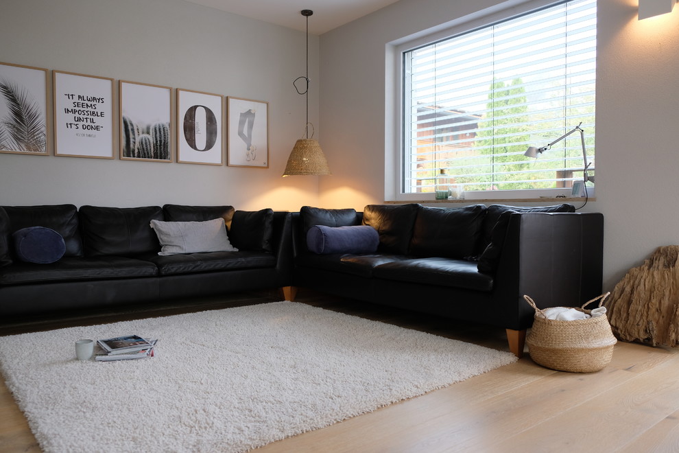 Modelo de sala de estar abierta escandinava de tamaño medio sin televisor con paredes grises, suelo de madera clara, estufa de leña y marco de chimenea de yeso