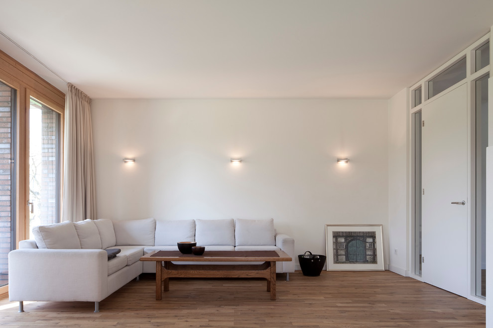 Diseño de sala de estar cerrada contemporánea de tamaño medio sin chimenea con paredes blancas y suelo de madera en tonos medios