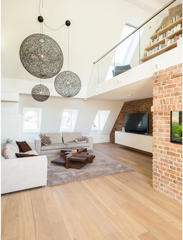 Идея дизайна: огромная двухуровневая гостиная комната в стиле лофт с с книжными шкафами и полками, белыми стенами, светлым паркетным полом, отдельно стоящим телевизором и коричневым полом без камина