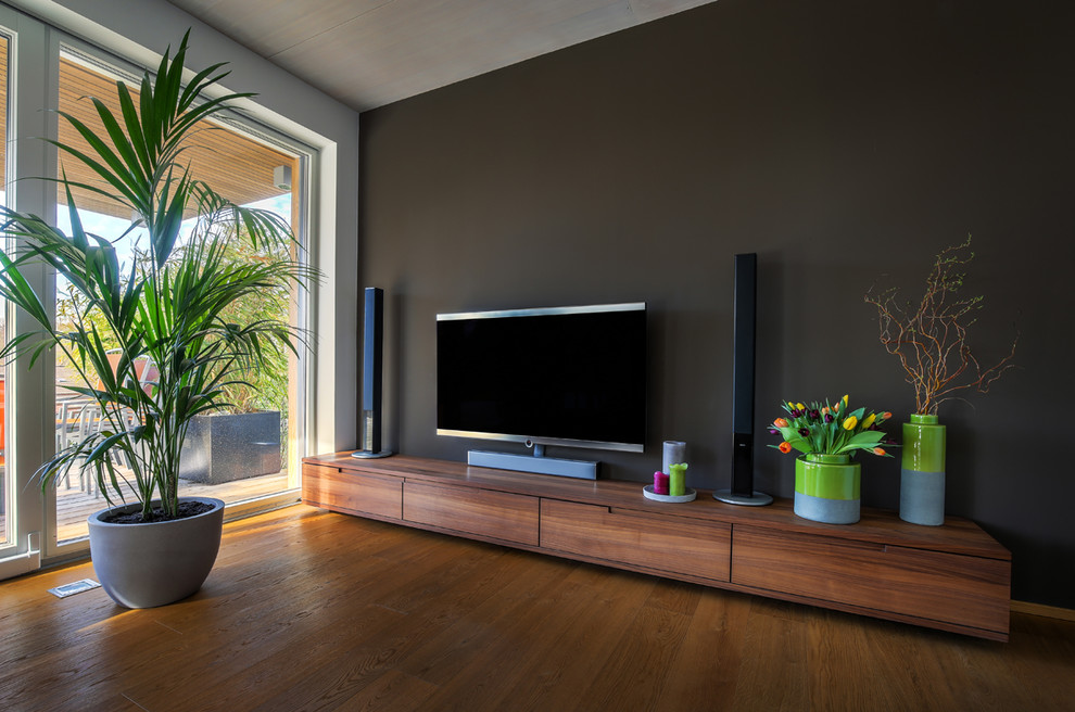 Großes, Abgetrenntes Modernes Wohnzimmer mit grauer Wandfarbe, gebeiztem Holzboden, freistehendem TV und braunem Boden in Köln