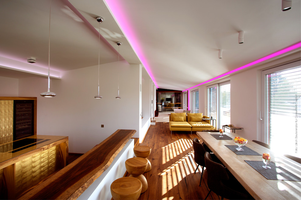 Ejemplo de salón abierto actual de tamaño medio con paredes blancas y suelo de madera en tonos medios