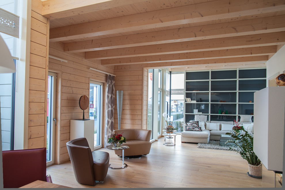Modelo de salón abierto actual extra grande con paredes marrones, suelo de madera clara, chimenea de doble cara y marco de chimenea de yeso