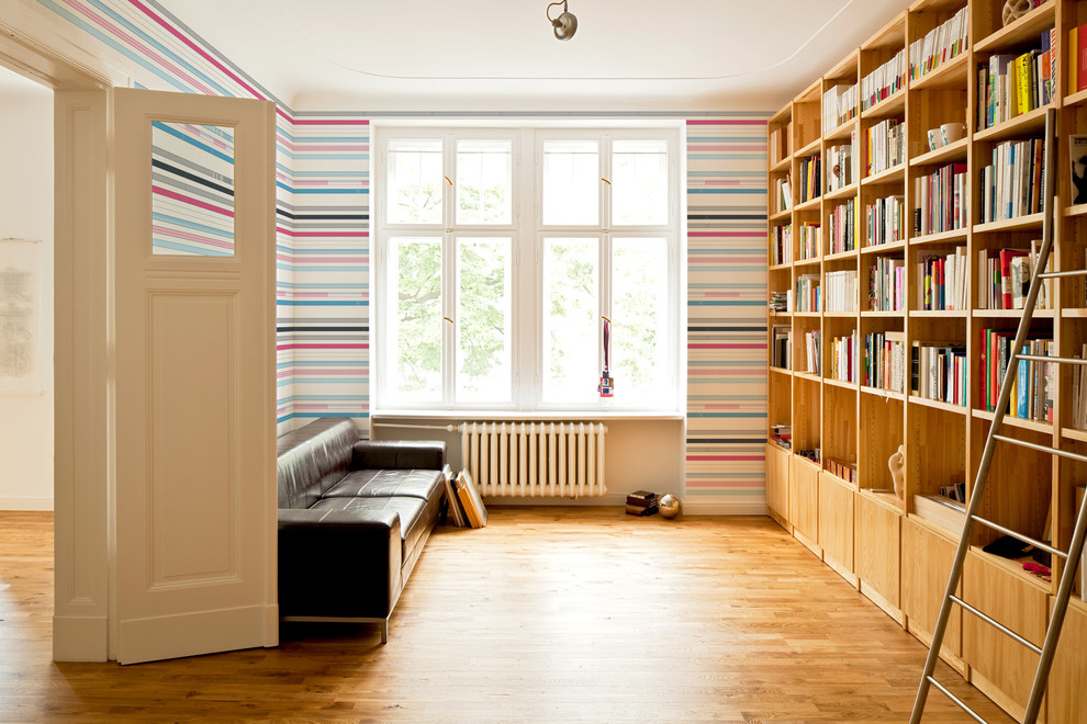Modern inredning av ett stort avskilt allrum, med ett bibliotek, flerfärgade väggar och mellanmörkt trägolv