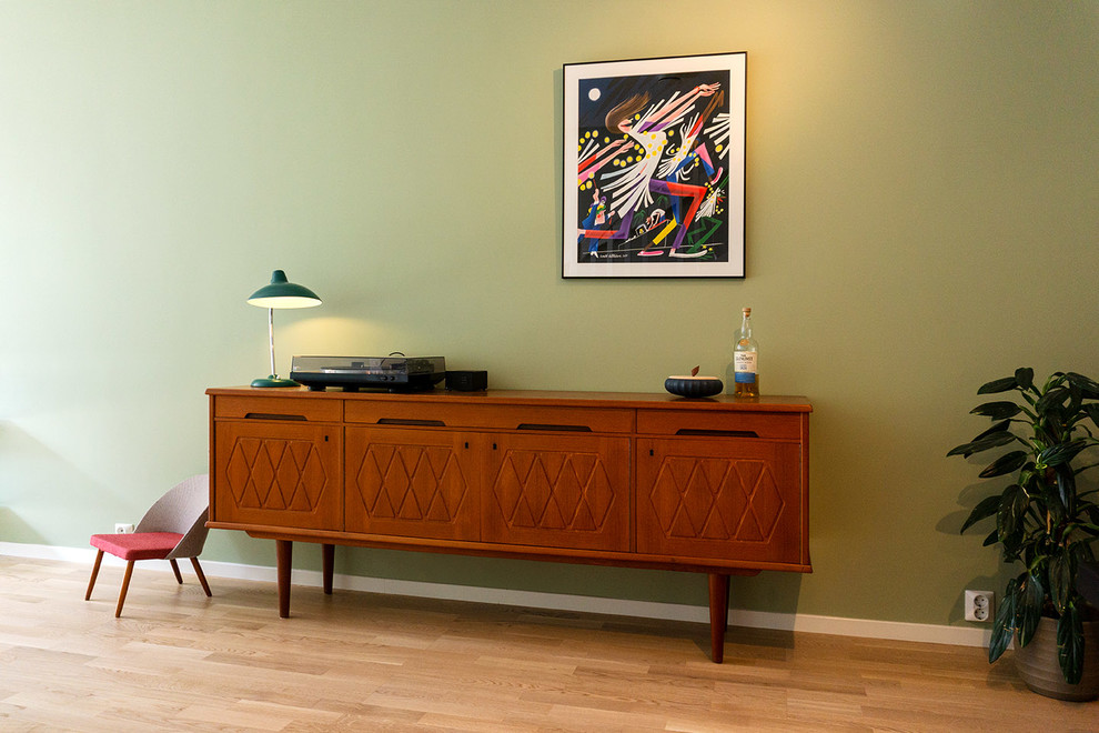 Modelo de sala de estar con rincón musical abierta nórdica de tamaño medio con paredes verdes, suelo de madera clara, televisor independiente y suelo beige