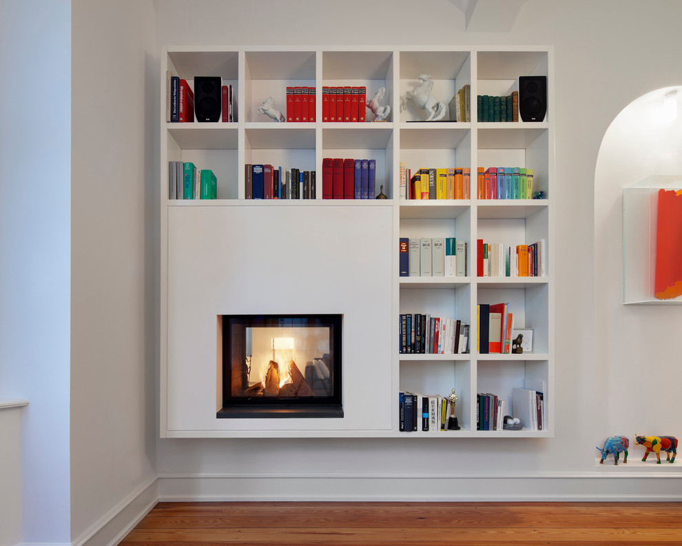 Aménagement d'un salon moderne avec une bibliothèque ou un coin lecture, un mur blanc, parquet peint, une cheminée double-face et un manteau de cheminée en plâtre.