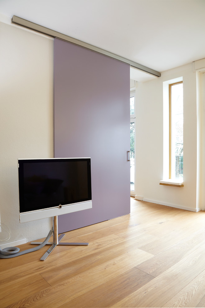 Modernes Wohnzimmer mit weißer Wandfarbe, hellem Holzboden und freistehendem TV in Essen