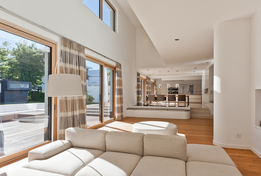 Modelo de salón abierto contemporáneo grande con paredes blancas y suelo de madera en tonos medios