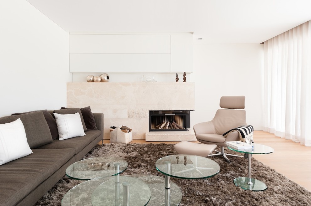 Стильный дизайн: большая гостиная комната в стиле модернизм с белыми стенами, светлым паркетным полом, стандартным камином, фасадом камина из камня и коричневым диваном без телевизора - последний тренд