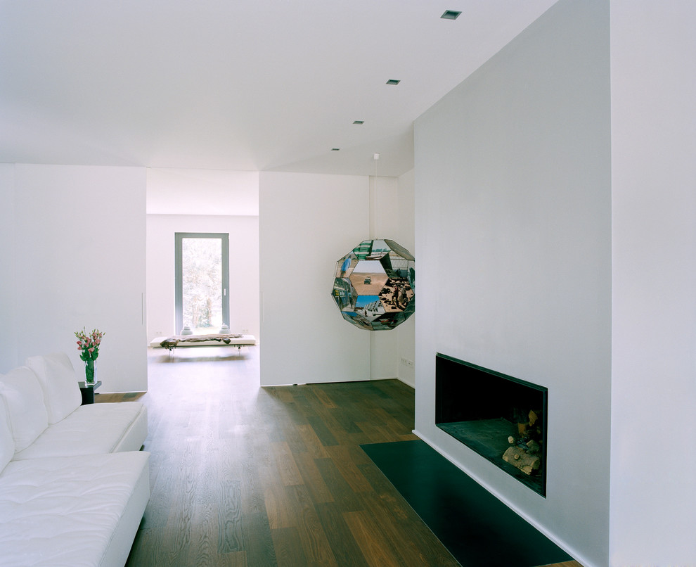 This is an example of a medium sized modern living room in Berlin with white walls, dark hardwood flooring, a standard fireplace and a plastered fireplace surround.