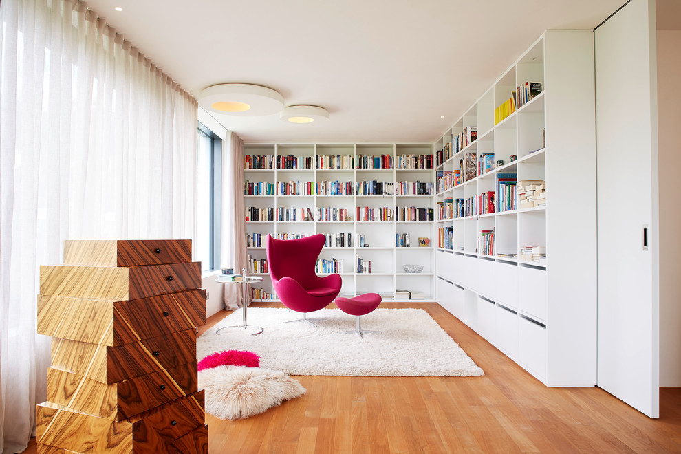 Cette image montre un salon design avec une bibliothèque ou un coin lecture, un sol en bois brun et éclairage.