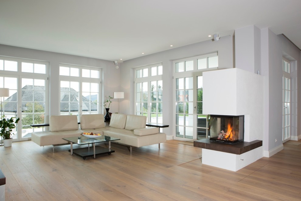 Aménagement d'un grand salon classique ouvert avec un mur gris, un sol en bois brun, une cheminée standard, un manteau de cheminée en plâtre et un téléviseur fixé au mur.