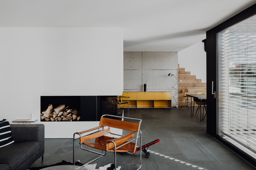 Idée de décoration pour une grande salle de séjour minimaliste avec un mur blanc, un sol en ardoise, un poêle à bois, un manteau de cheminée en plâtre et un sol noir.