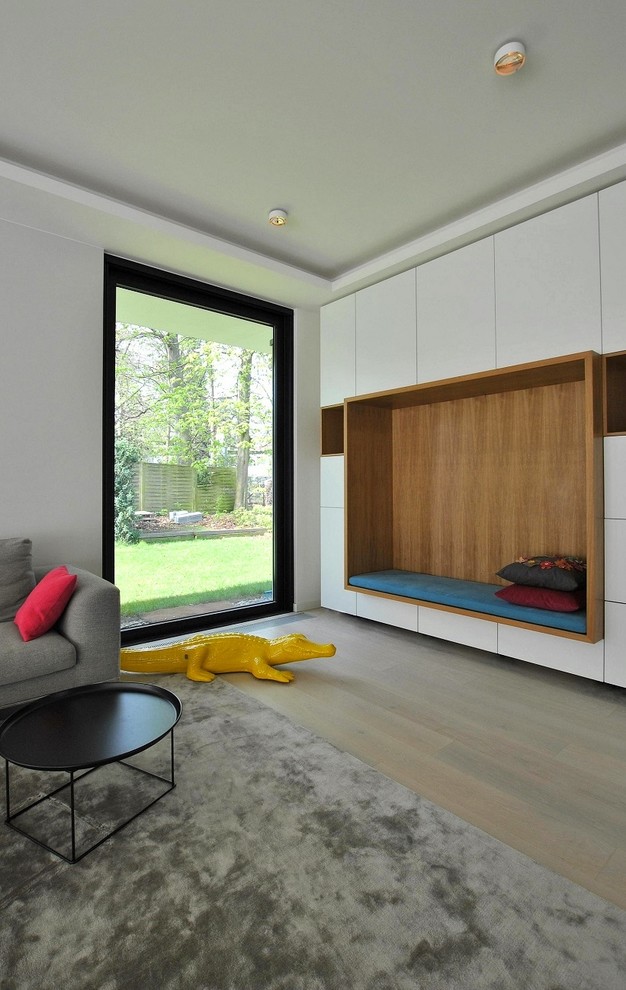 Ejemplo de sala de estar con biblioteca abierta minimalista de tamaño medio sin chimenea y televisor con paredes blancas, suelo de madera clara y suelo marrón