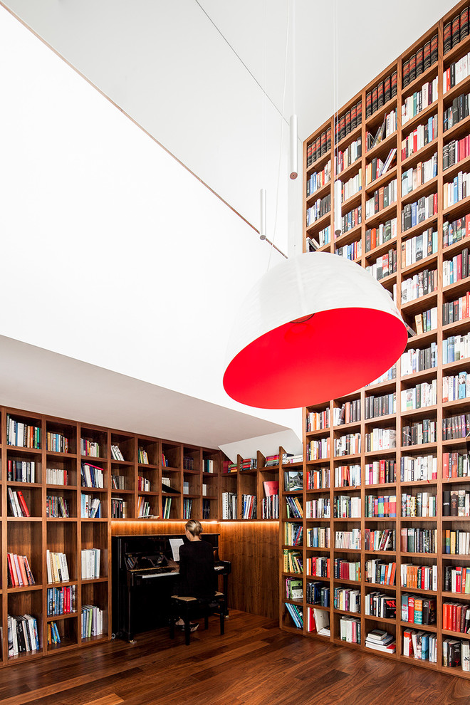 Cette image montre une salle de séjour minimaliste de taille moyenne et fermée avec une bibliothèque ou un coin lecture, un mur blanc, un sol en bois brun, un sol marron, aucune cheminée et aucun téléviseur.