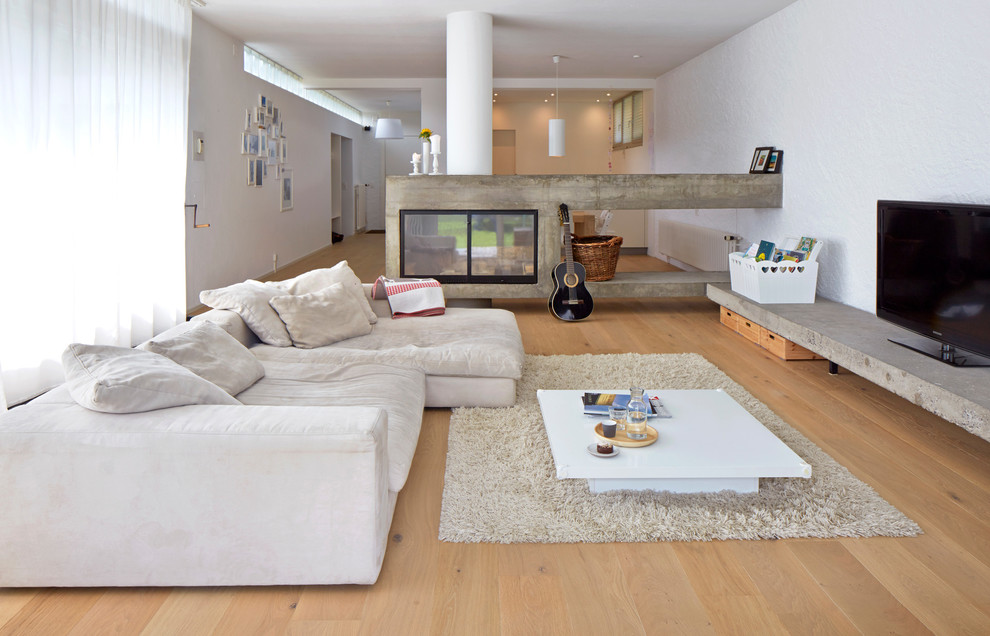Bild på ett stort industriellt vardagsrum, med mellanmörkt trägolv, brunt golv, ett musikrum, vita väggar, en dubbelsidig öppen spis och en fristående TV