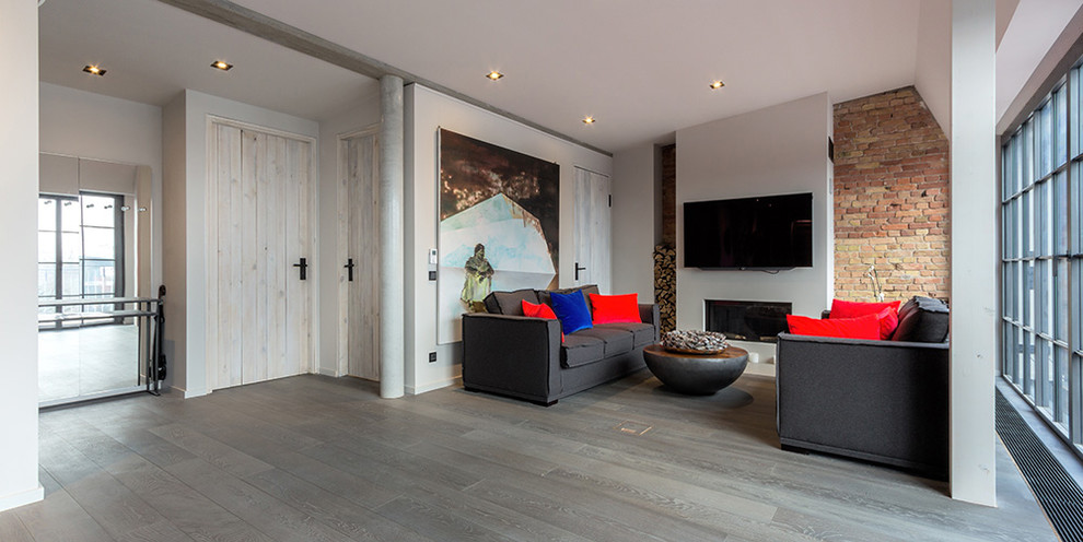 Großes Modernes Wohnzimmer im Loft-Stil mit grauer Wandfarbe, gebeiztem Holzboden, Kamin, verputzter Kaminumrandung, TV-Wand und braunem Boden in Berlin