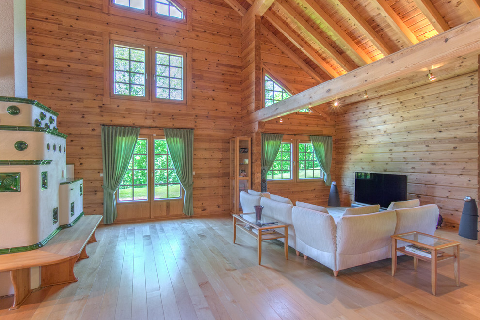 Imagen de salón abierto rural grande con suelo de madera clara, televisor independiente, paredes marrones, estufa de leña y marco de chimenea de baldosas y/o azulejos