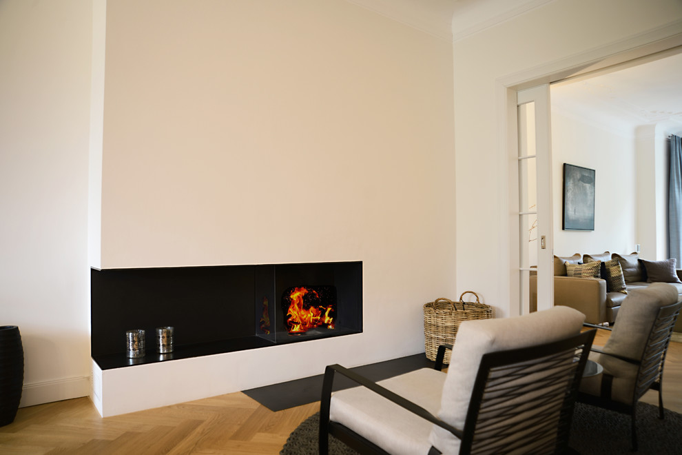 ハンブルクにある高級な中くらいなコンテンポラリースタイルのおしゃれなリビング (コーナー設置型暖炉、漆喰の暖炉まわり、白い壁、淡色無垢フローリング) の写真