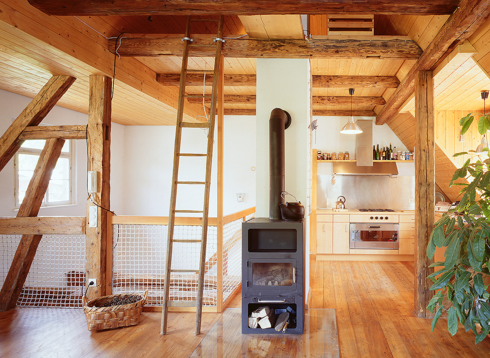 Imagen de salón abierto rústico con paredes blancas, suelo de madera en tonos medios y estufa de leña