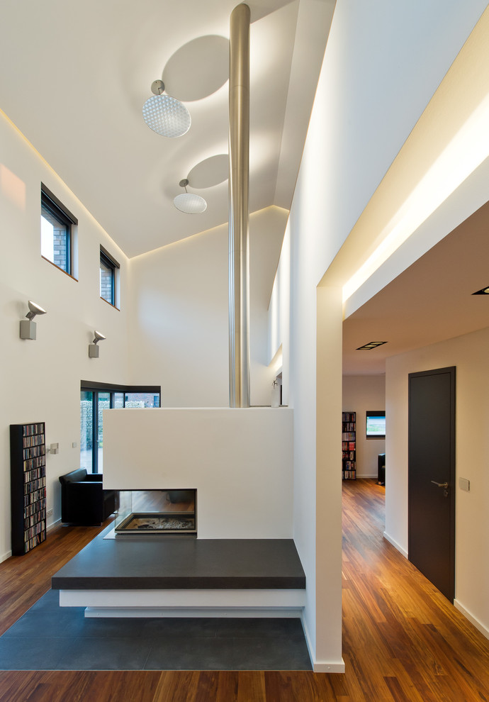 Offenes Modernes Wohnzimmer mit weißer Wandfarbe, braunem Holzboden, Tunnelkamin und verputzter Kaminumrandung in Hannover