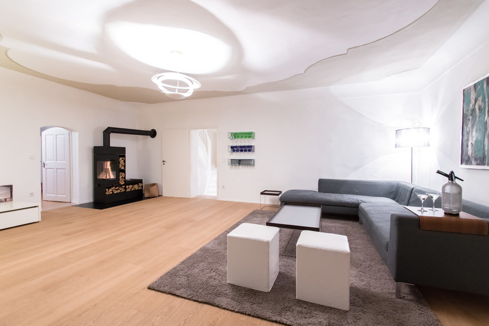 Idée de décoration pour un grand salon minimaliste ouvert avec un mur blanc, parquet clair, une salle de réception et un poêle à bois.