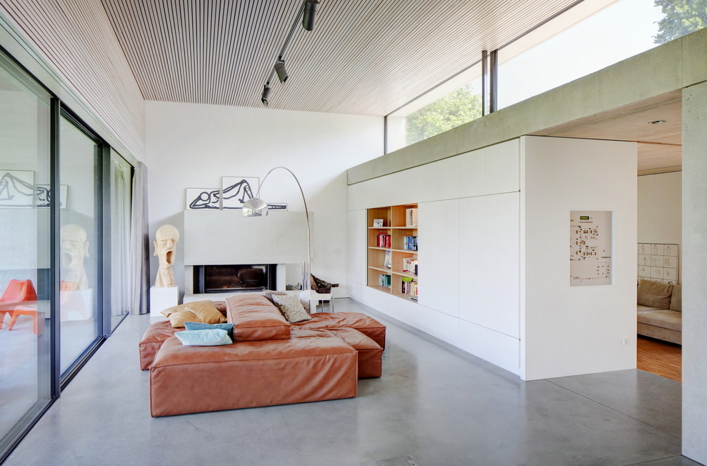 Ejemplo de salón abierto contemporáneo de tamaño medio sin televisor con paredes blancas, suelo de cemento, chimenea lineal y marco de chimenea de yeso