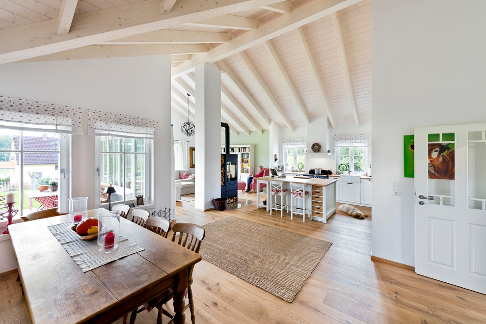 This is an example of a large rural open plan living room in Nuremberg with white walls, light hardwood flooring, a wood burning stove, a metal fireplace surround, a freestanding tv and brown floors.