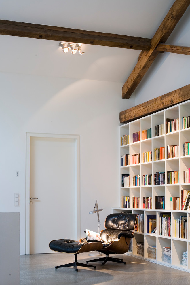 Cette image montre une salle de séjour design de taille moyenne et fermée avec une bibliothèque ou un coin lecture, un mur blanc, sol en béton ciré, aucune cheminée, aucun téléviseur et un sol gris.