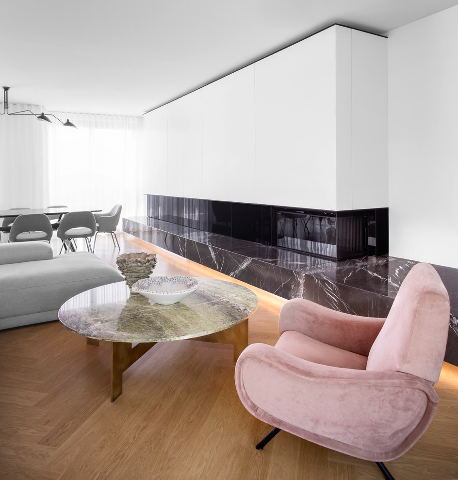 Foto de sala de estar abierta minimalista grande con paredes blancas, suelo de madera clara, marco de chimenea de piedra y chimenea lineal