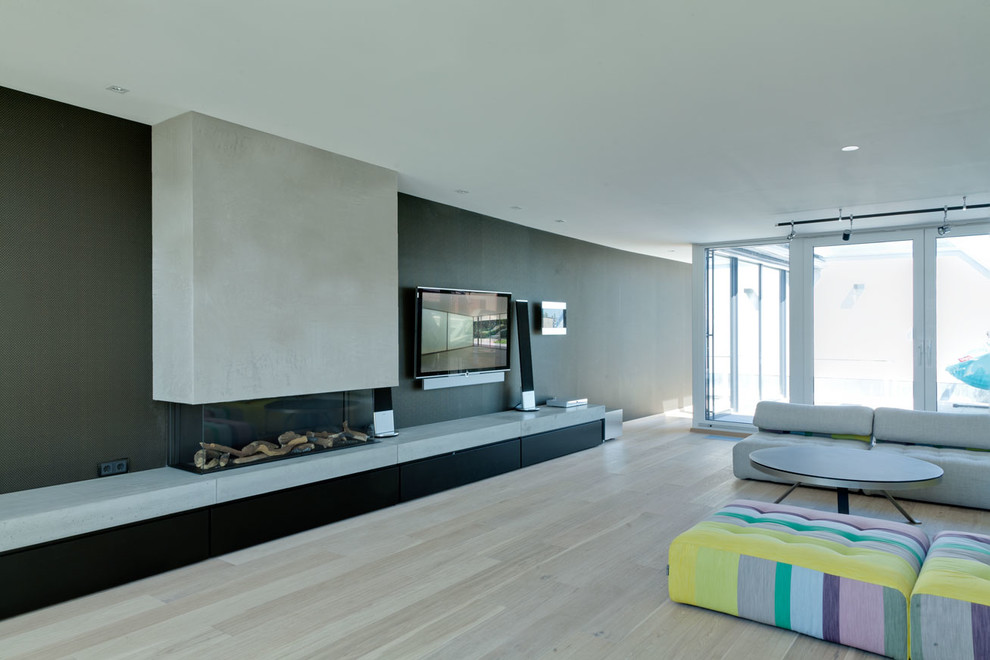 Idee per un soggiorno contemporaneo aperto con pareti nere, parquet chiaro, camino lineare Ribbon, cornice del camino in cemento e TV a parete
