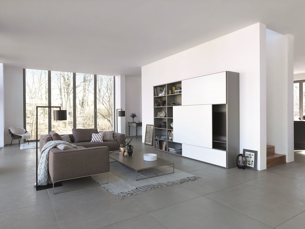 Modelo de sala de estar con biblioteca abierta contemporánea grande sin chimenea con paredes blancas, televisor retractable y suelo gris