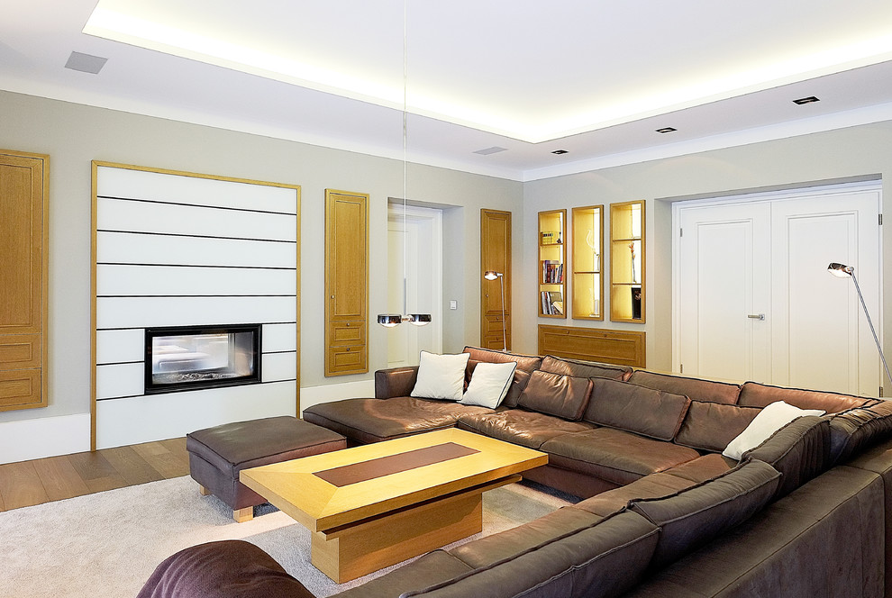 Cette image montre une très grande salle de séjour design fermée avec un mur gris, une cheminée double-face, un sol en bois brun, un manteau de cheminée en bois, un téléviseur indépendant et un sol marron.