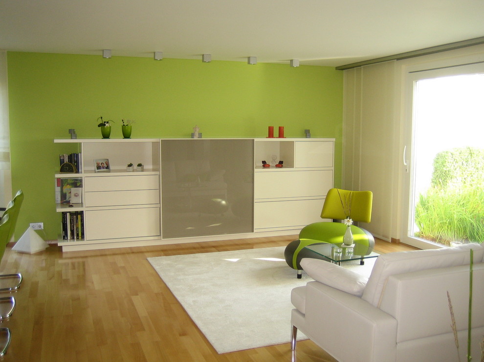 Foto de salón abierto contemporáneo de tamaño medio con suelo de madera clara, suelo marrón, paredes verdes y televisor retractable