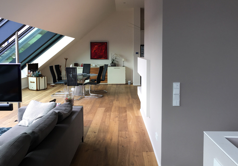 Imagen de sala de estar abierta actual grande sin chimenea con paredes grises, suelo de madera clara, televisor independiente y suelo marrón