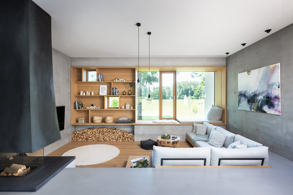 This is an example of an expansive scandinavian open plan games room in Munich with white walls, concrete flooring, a hanging fireplace, a metal fireplace surround, a wall mounted tv and grey floors.