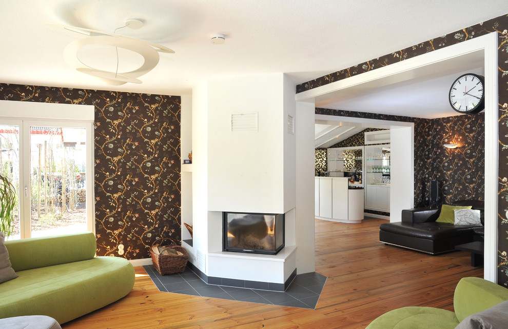 Ejemplo de sala de estar abierta contemporánea extra grande con paredes multicolor, marco de chimenea de yeso, todas las chimeneas y suelo de madera en tonos medios