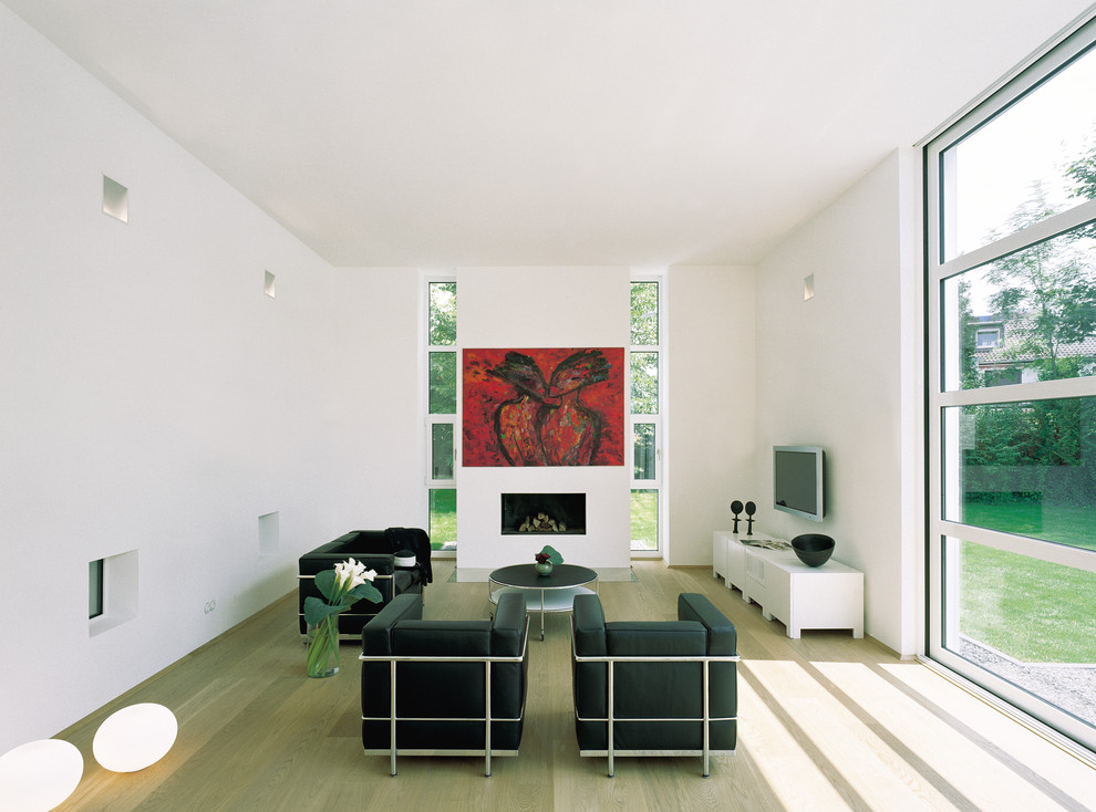 Imagen de sala de estar abierta contemporánea de tamaño medio con paredes blancas, suelo de madera clara, todas las chimeneas, televisor colgado en la pared y marco de chimenea de yeso