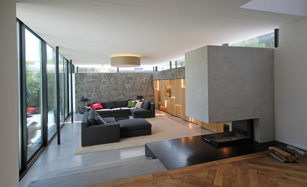 Inspiration for a large contemporary formal open plan living room in Munich with grey walls, concrete flooring, a concrete fireplace surround, a concealed tv, grey floors, a two-sided fireplace and feature lighting.
