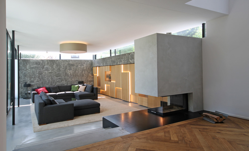 Пример оригинального дизайна: большая двухуровневая гостиная комната в современном стиле с серыми стенами, бетонным полом, фасадом камина из бетона, скрытым телевизором, серым полом и двусторонним камином