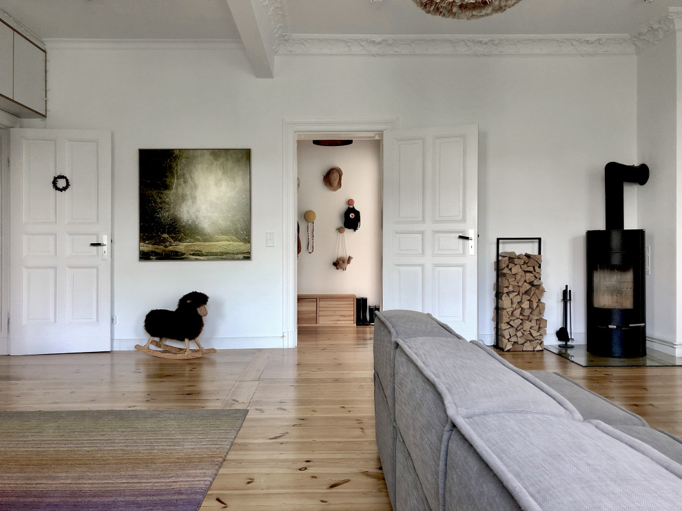 Foto de sala de estar abierta actual de tamaño medio con paredes blancas, suelo de madera clara, estufa de leña, marco de chimenea de yeso y suelo marrón