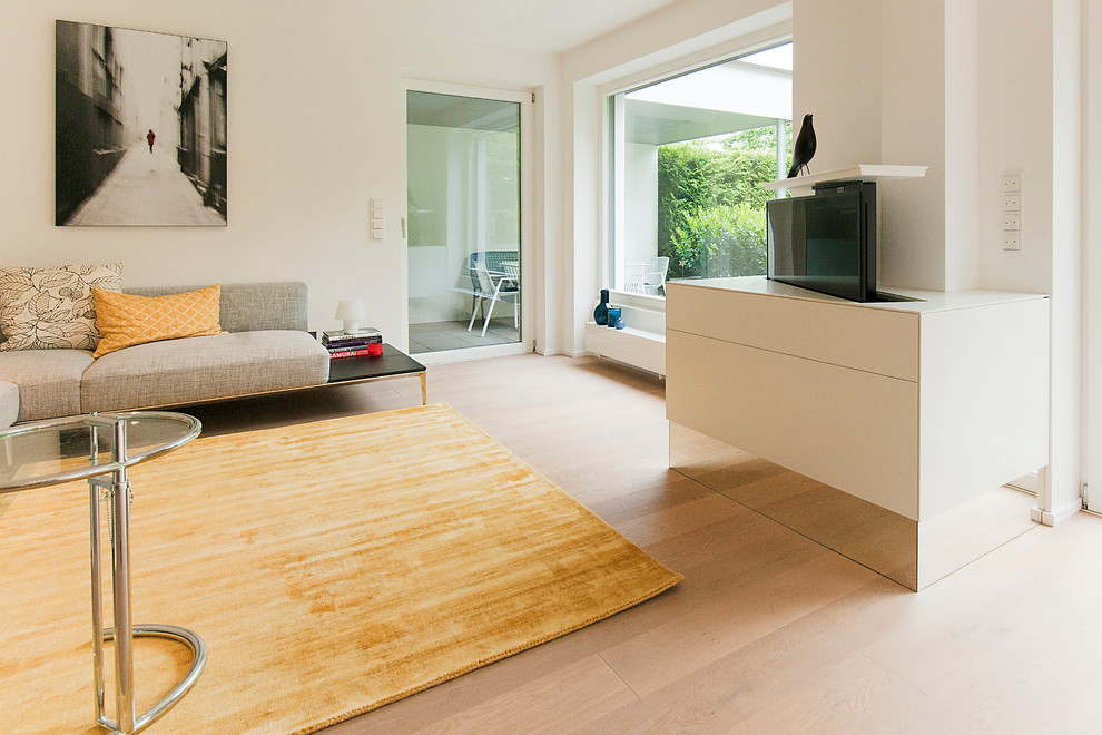 Immagine di un soggiorno design di medie dimensioni e aperto con pareti bianche, parquet chiaro, TV nascosta e pavimento marrone