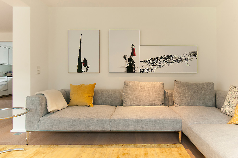 Cette image montre une salle de séjour design de taille moyenne et ouverte avec un mur blanc, parquet clair, un téléviseur dissimulé et un sol marron.