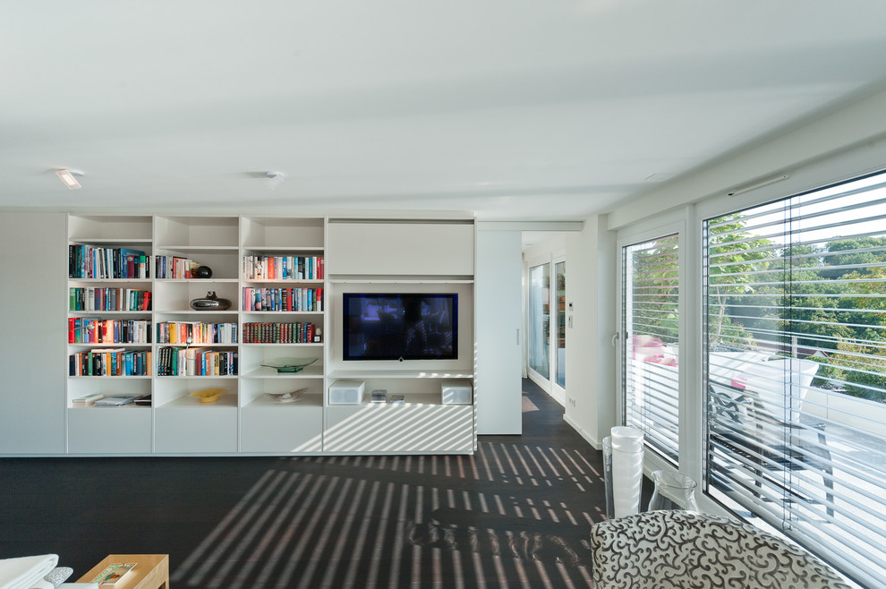 Imagen de salón para visitas tipo loft moderno grande con paredes blancas, suelo de madera oscura, chimeneas suspendidas y televisor retractable