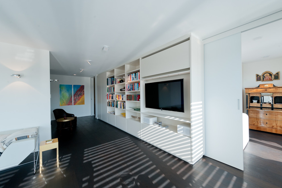 Diseño de biblioteca en casa abierta minimalista grande con suelo de madera oscura y televisor colgado en la pared