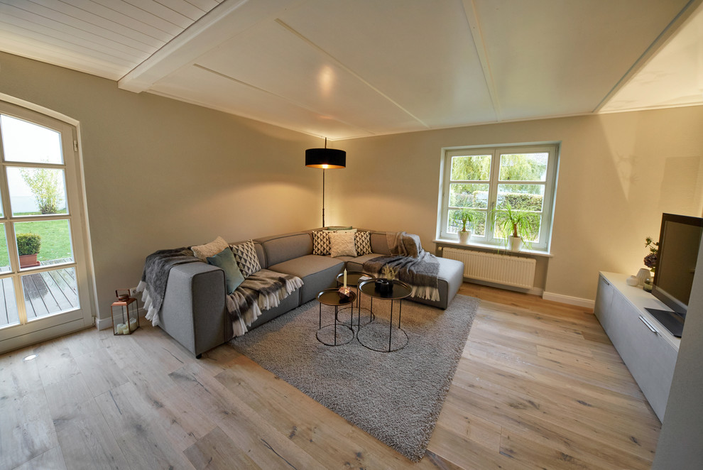 Mittelgroßes Modernes Wohnzimmer mit grauer Wandfarbe, hellem Holzboden und freistehendem TV in München