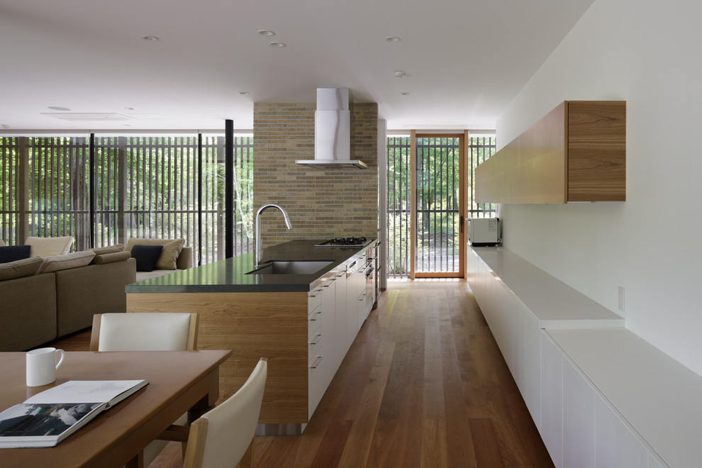 Immagine di una cucina moderna con lavello sottopiano, ante a filo, ante nere, top in quarzo composito, elettrodomestici in acciaio inossidabile, pavimento in legno massello medio, pavimento arancione e top bianco