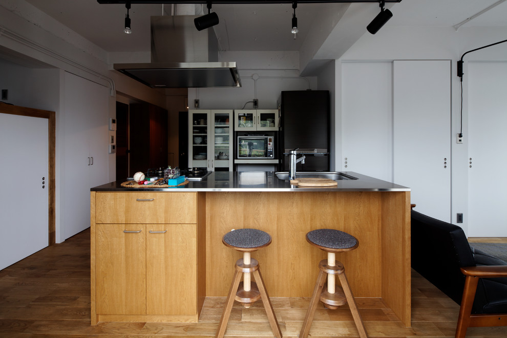 Foto på ett industriellt linjärt kök med öppen planlösning, med en enkel diskho, släta luckor, skåp i mellenmörkt trä, bänkskiva i rostfritt stål, mellanmörkt trägolv, en köksö och brunt golv