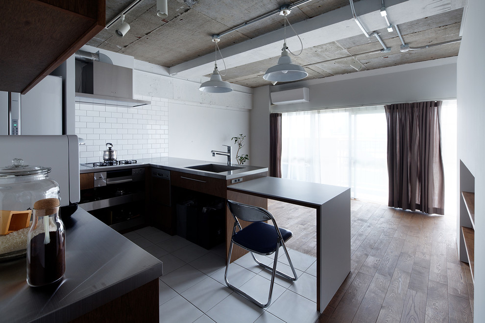 Industrial Wohnküche in U-Form mit Küchenrückwand in Weiß, Rückwand aus Metrofliesen, braunem Holzboden, flächenbündigen Schrankfronten, schwarzen Schränken, Edelstahl-Arbeitsplatte und Kücheninsel in Sonstige