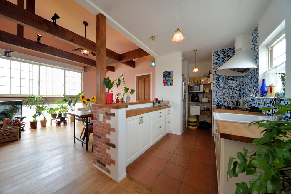 Design ideas for a world-inspired single-wall open plan kitchen in Other with a belfast sink, raised-panel cabinets, white cabinets, wood worktops, terracotta flooring, a breakfast bar and brown floors.